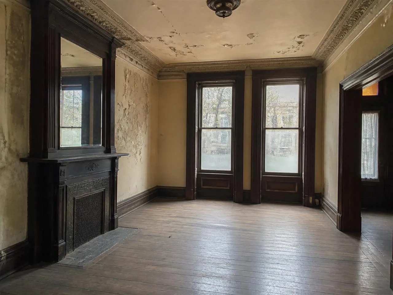 Brownstone renovation Brooklyn before photo of an unrestored parlor floor with peeling plaster and worn heart pine floors