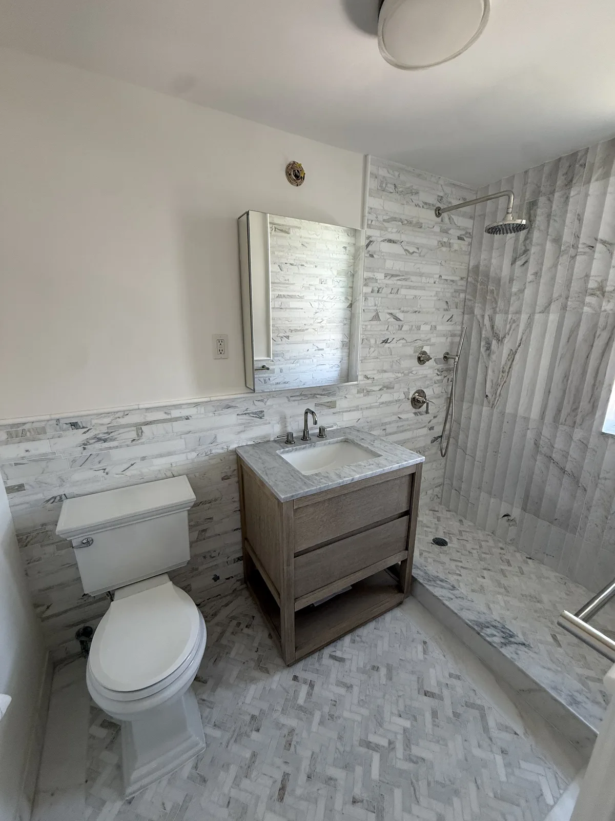 Completed bathroom renovation with marble subway tile and wood vanity in New York City