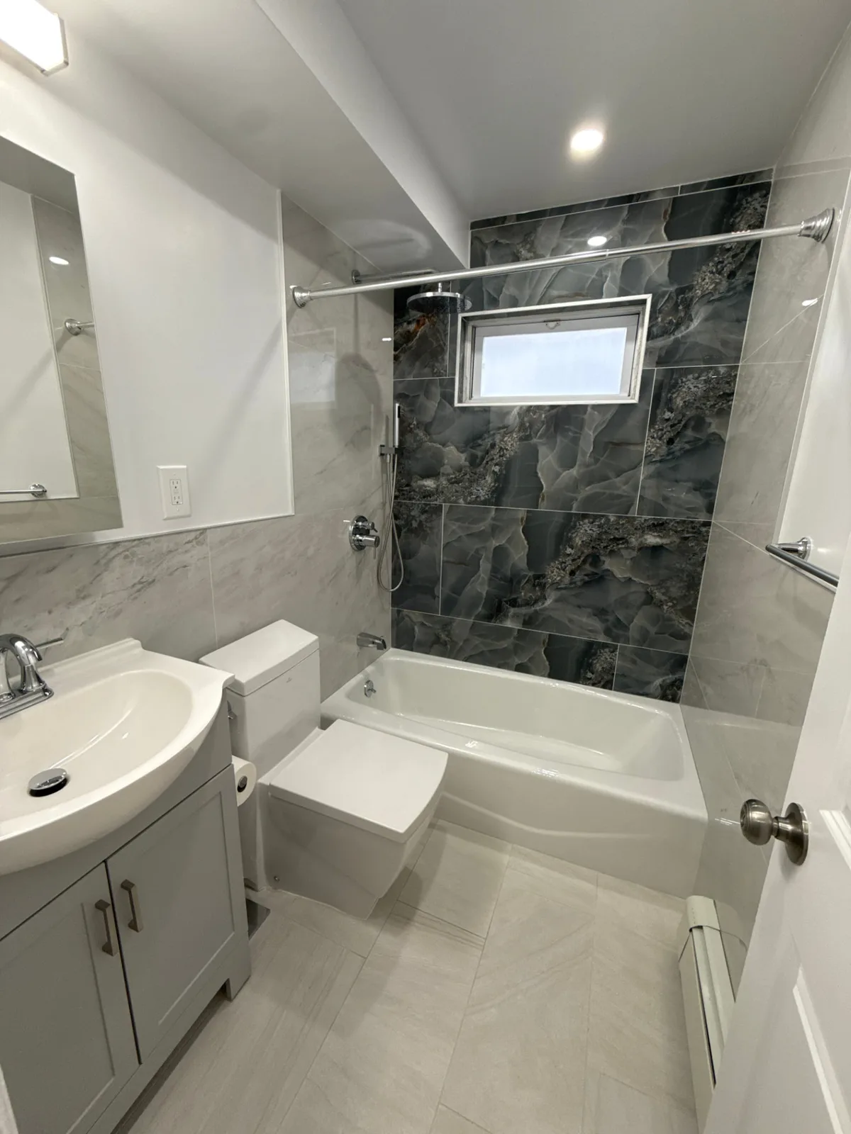 Bathroom renovation with dark marble accent wall and soaking tub in New York City