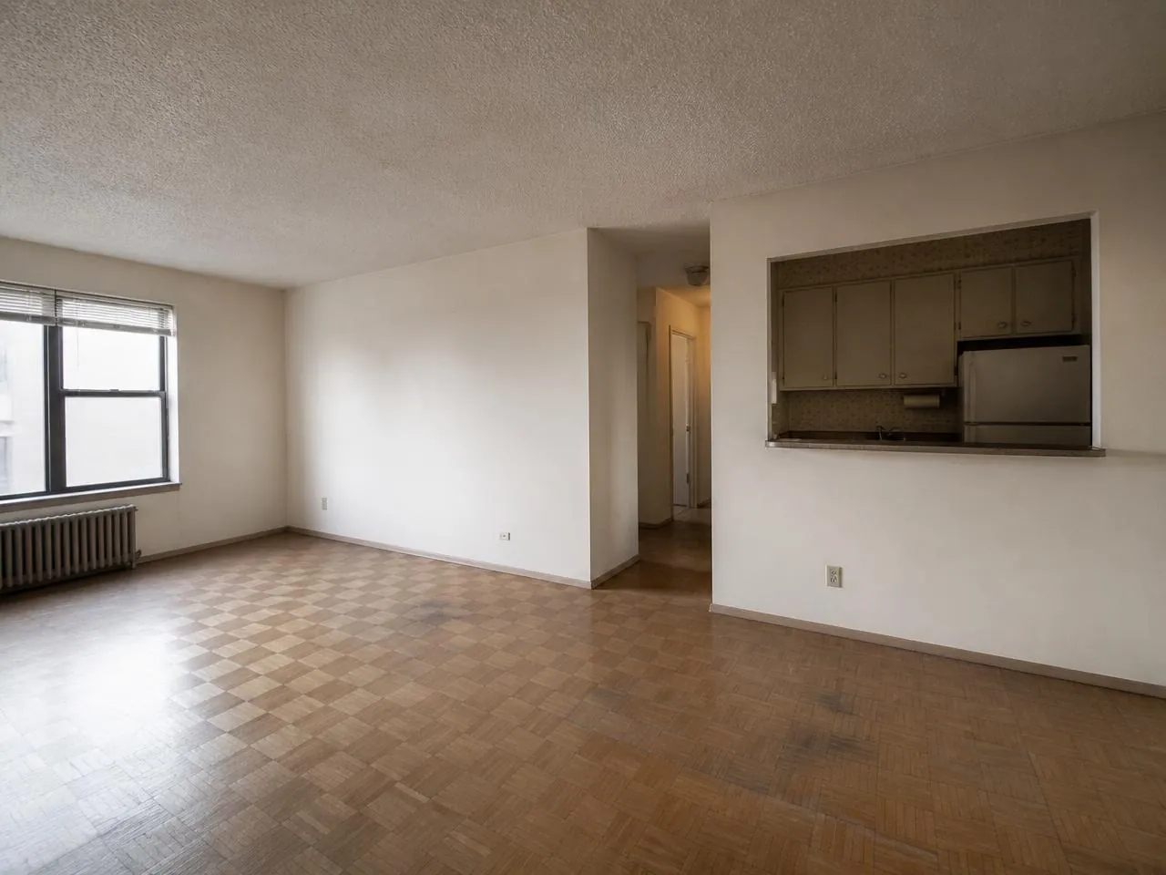 Co-op renovation NYC before photo — dated post-war apartment with parquet floors and original kitchen pass-through