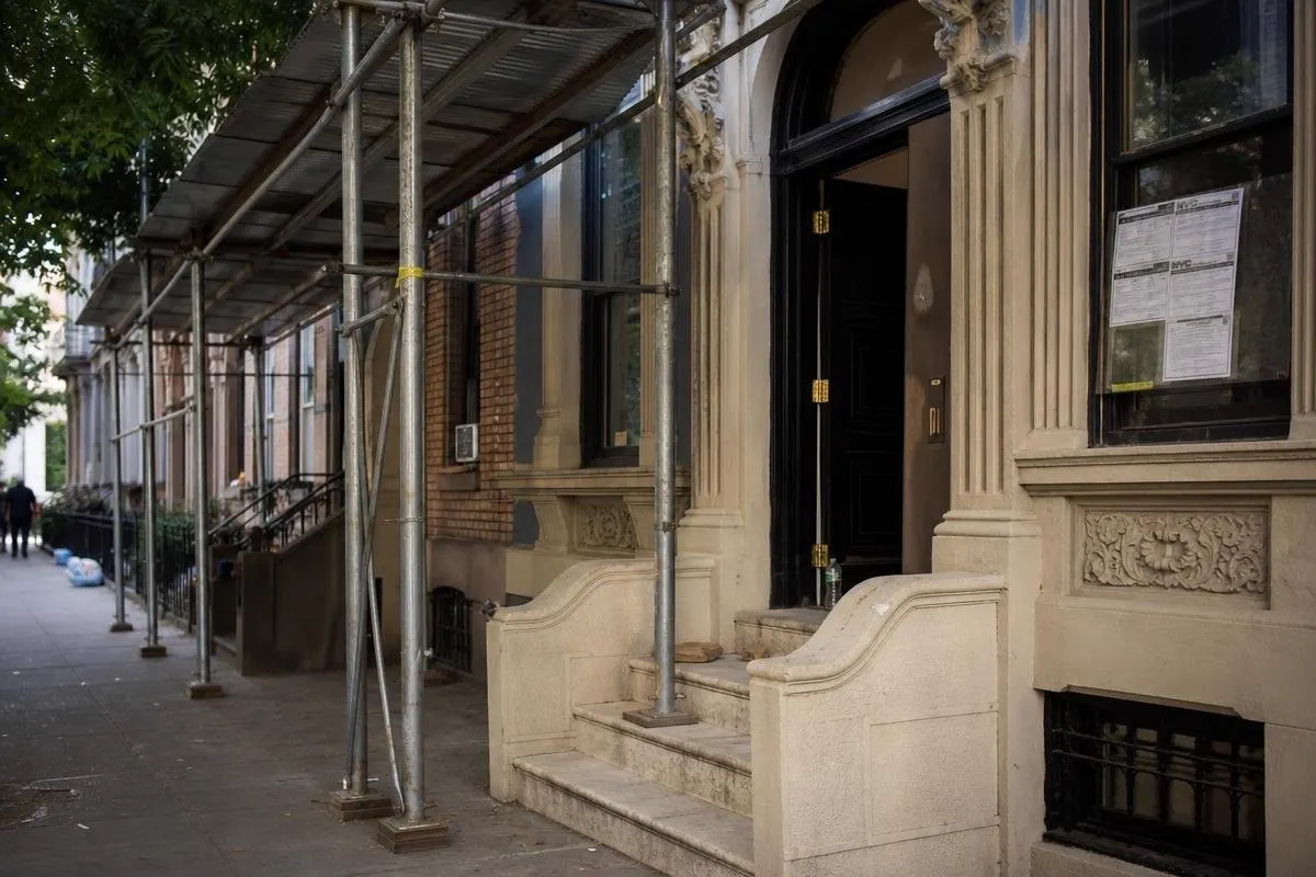 A brownstone building in Brooklyn with scaffolding on the sidewalk and a permit posted on the window