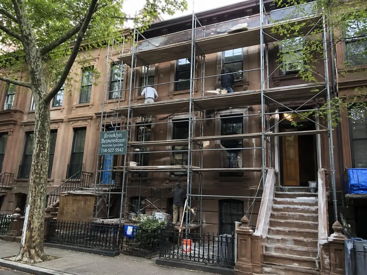 Brownstone facade restoration in Brooklyn with scaffolding, repointed mortar joints, and stoop rebuild in progress