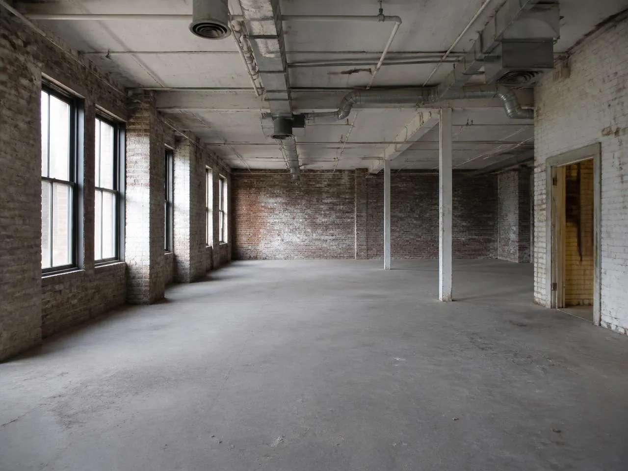 Before a loft renovation NYC with raw concrete floor, exposed brick and open industrial ductwork