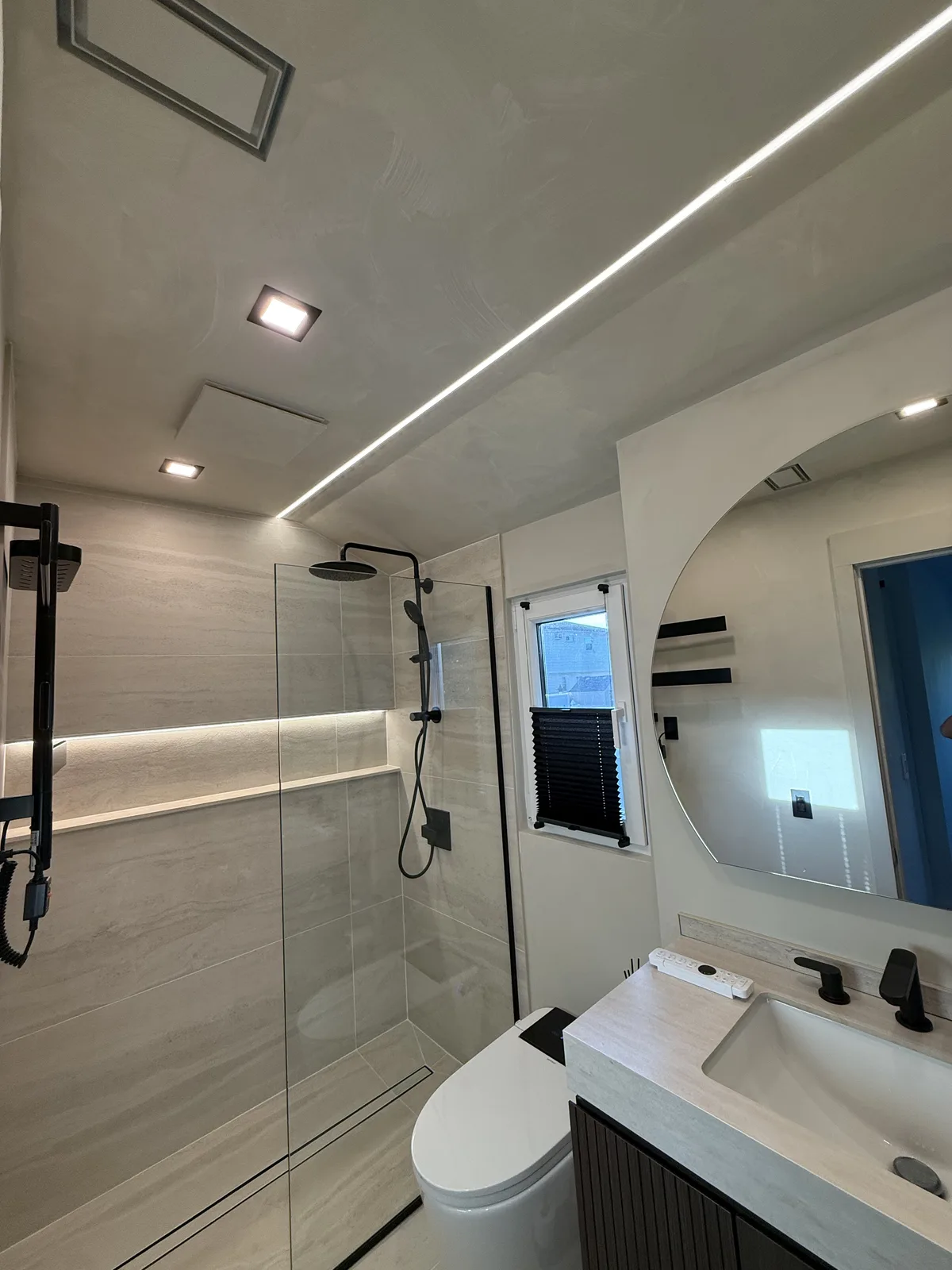 Modern bathroom renovation with LED ceiling strip, round mirror and walk-in shower in New York City
