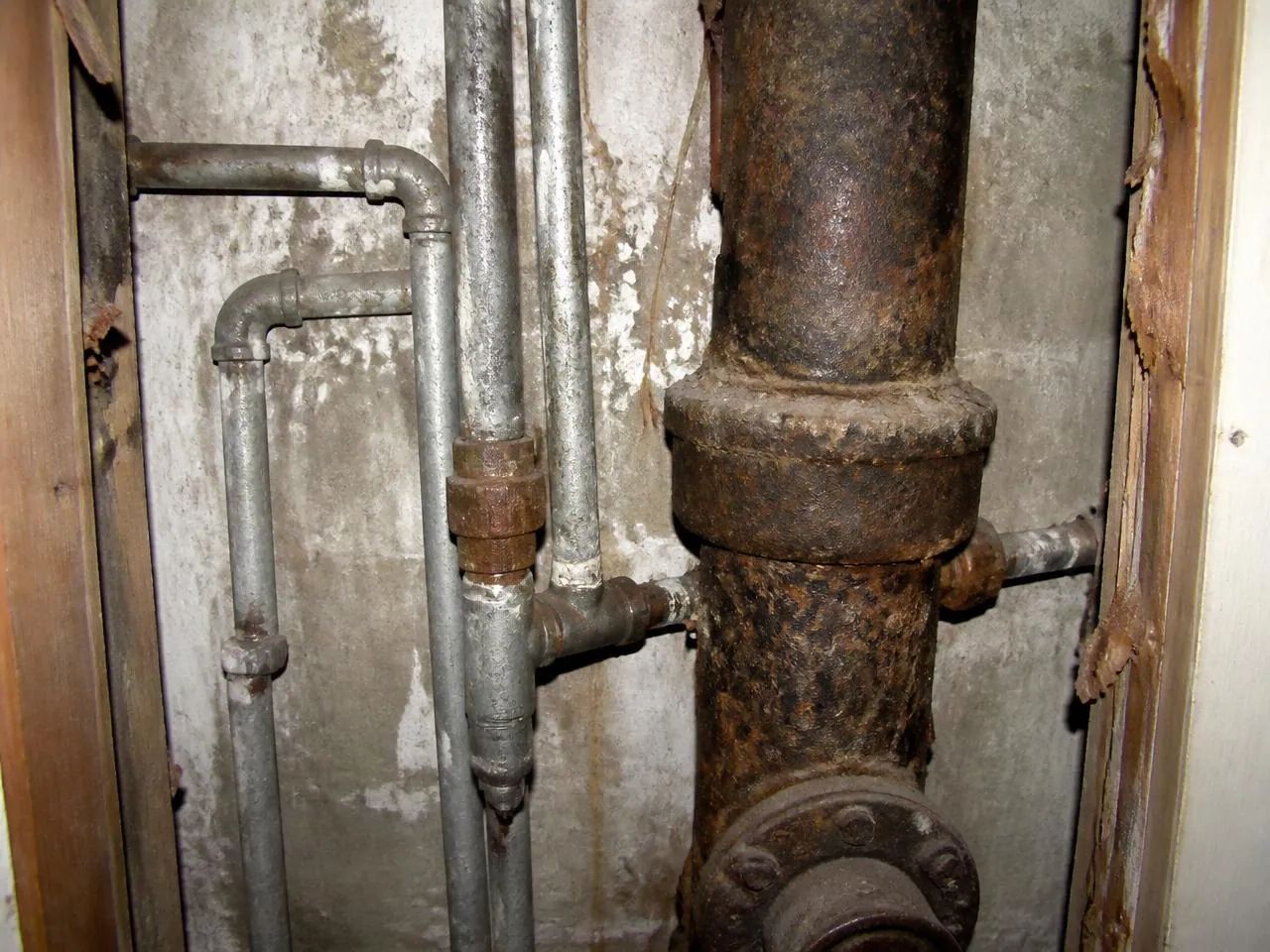Corroded galvanized supply lines and cast iron drain stack in a pre-war NYC building before pipe replacement