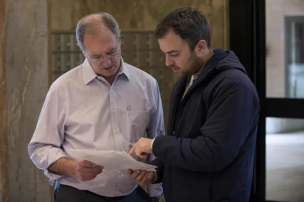 Two men reviewing co-op alteration agreement documents together in a Brooklyn building lobby