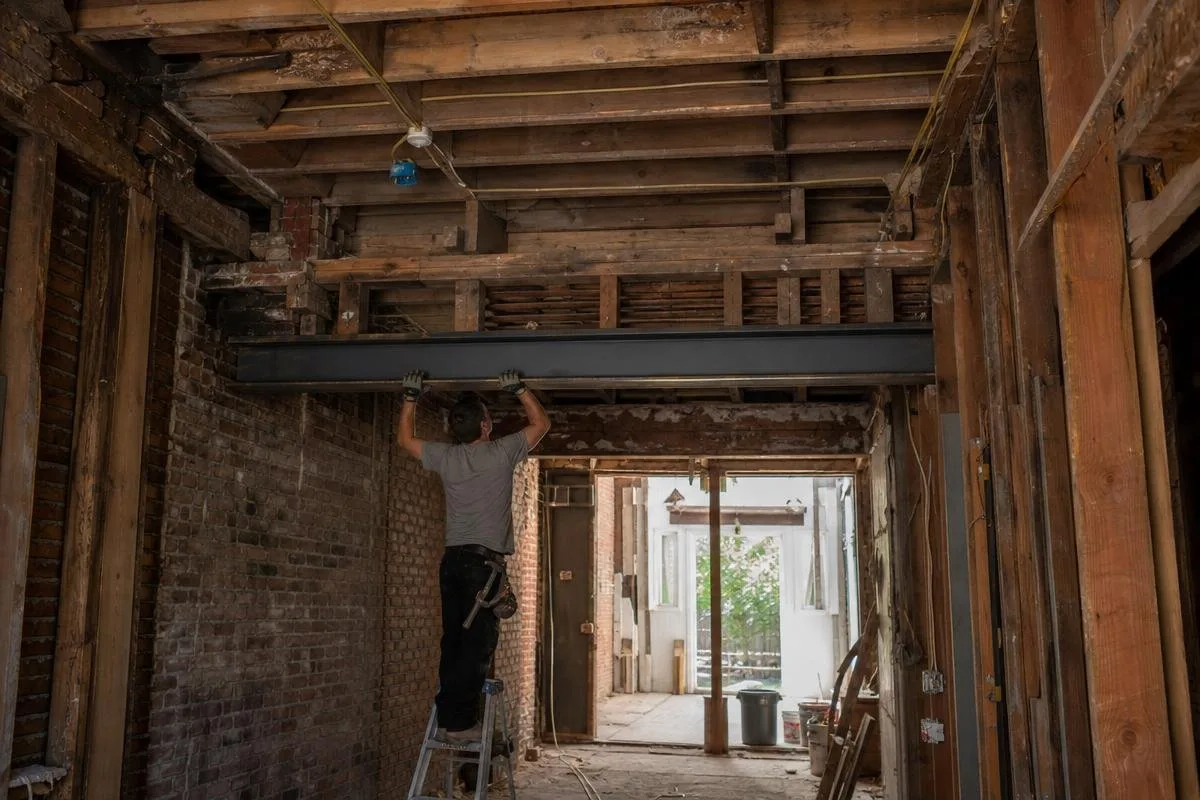 Worker beneath exposed ceiling joists and a steel beam in a stripped interior