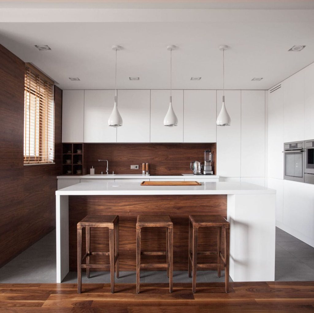 Modern kitchen with white cabinets, wood accents, a large island with three wooden stools, pendant lights, and built-in appliances.